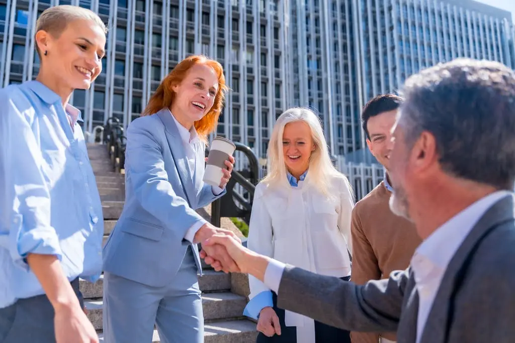 woman and a man shaking hands in front of corporate building